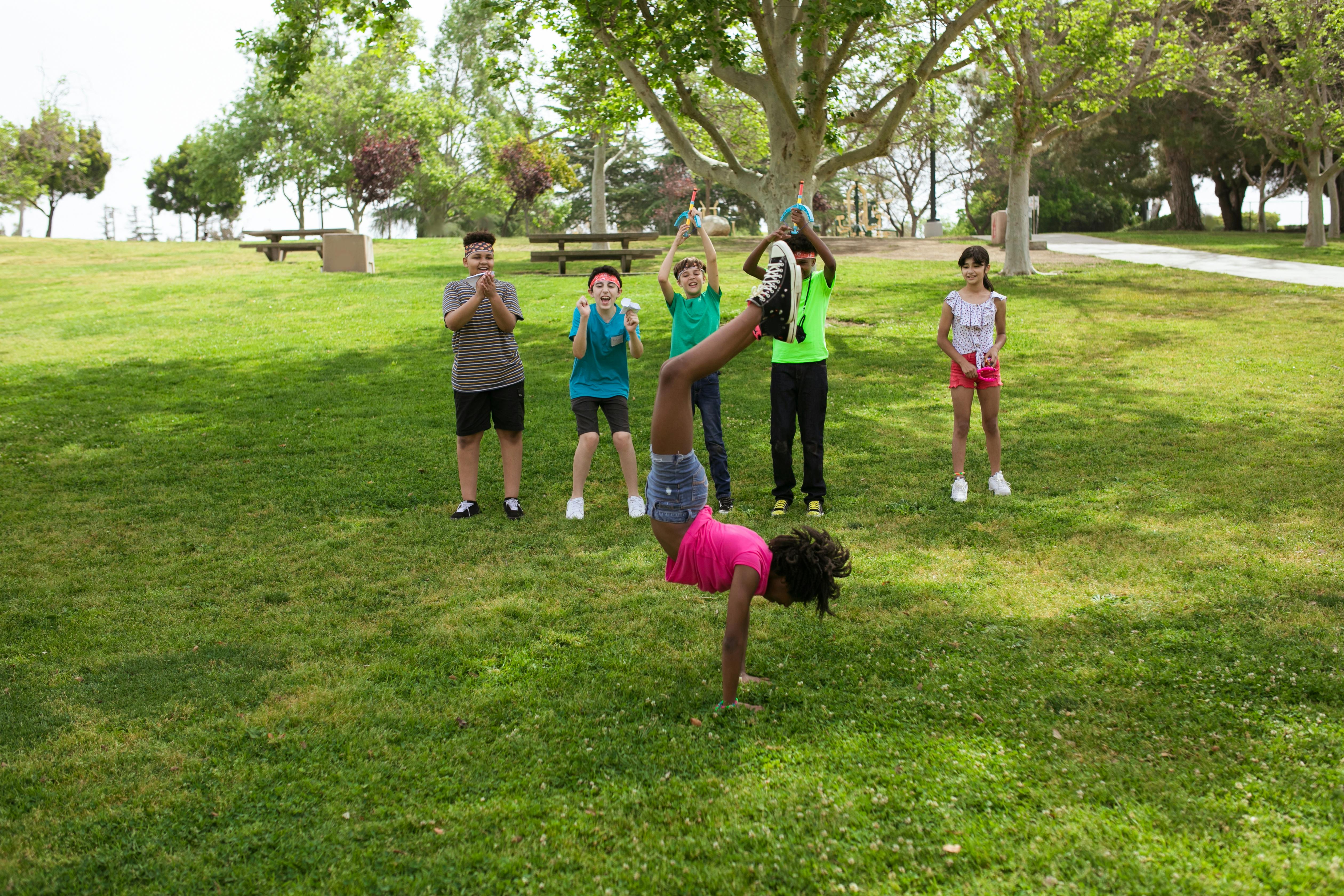 Young Black girl doing a handstand in front of three boys and one girl who are cheering