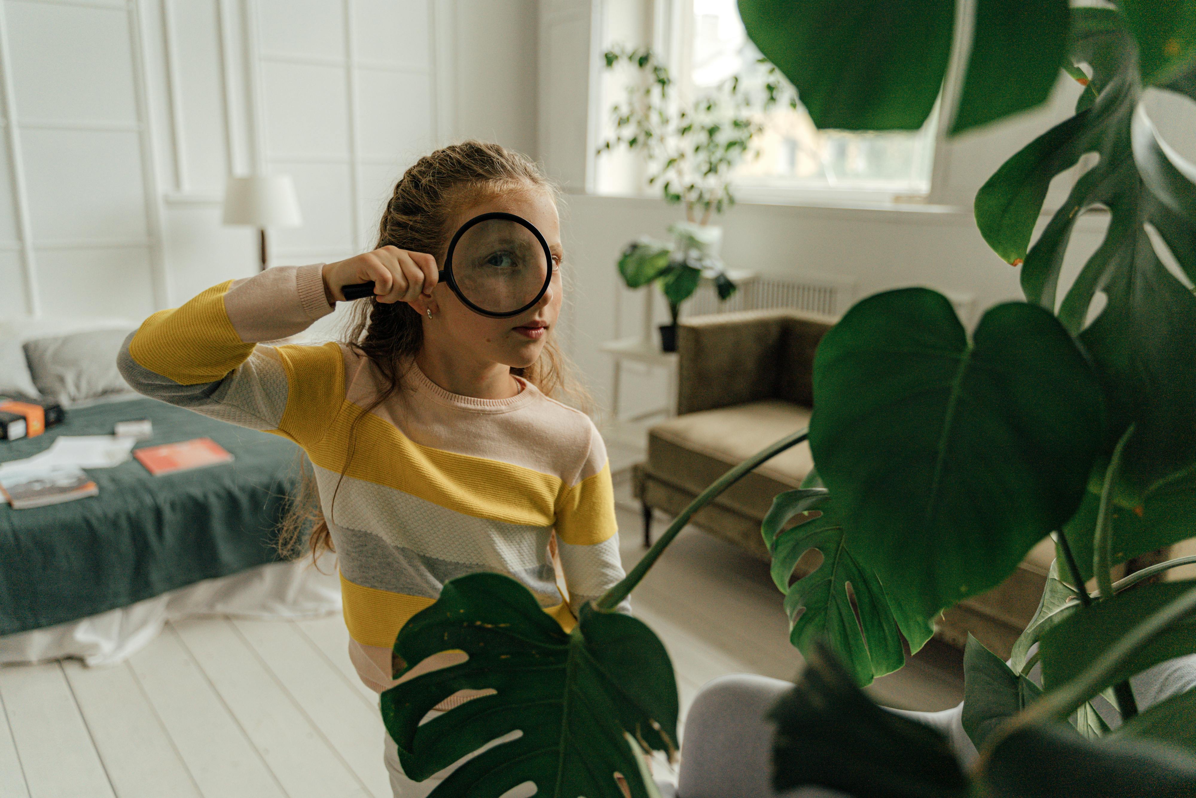 Young blonde girl looking through a magnifying glass at a fern